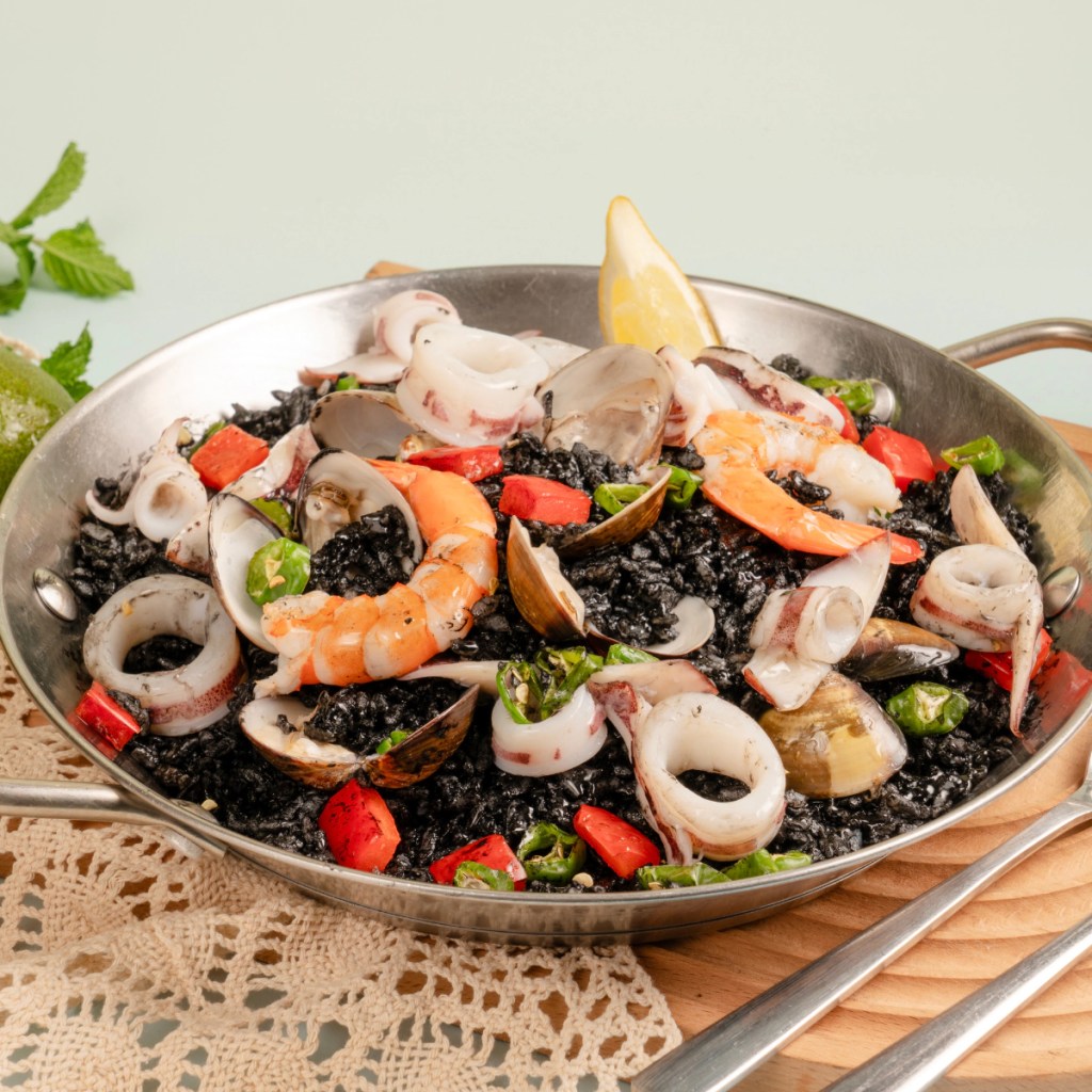 「濃醇黑浪墨魚燉飯」以自製海鮮高湯與墨魚汁燉煮米飯,搭配蛤蜊、新鮮墨魚及帕瑪森起司,呈現深厚鮮濃滋味。(圖片提供:金色三麥)